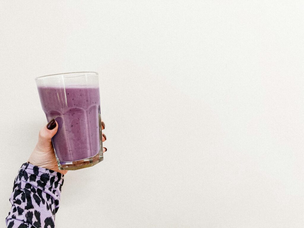 A person's hand holding a healthy purple smoothie in a glass with a white background. Perfect for health and wellness themes.
